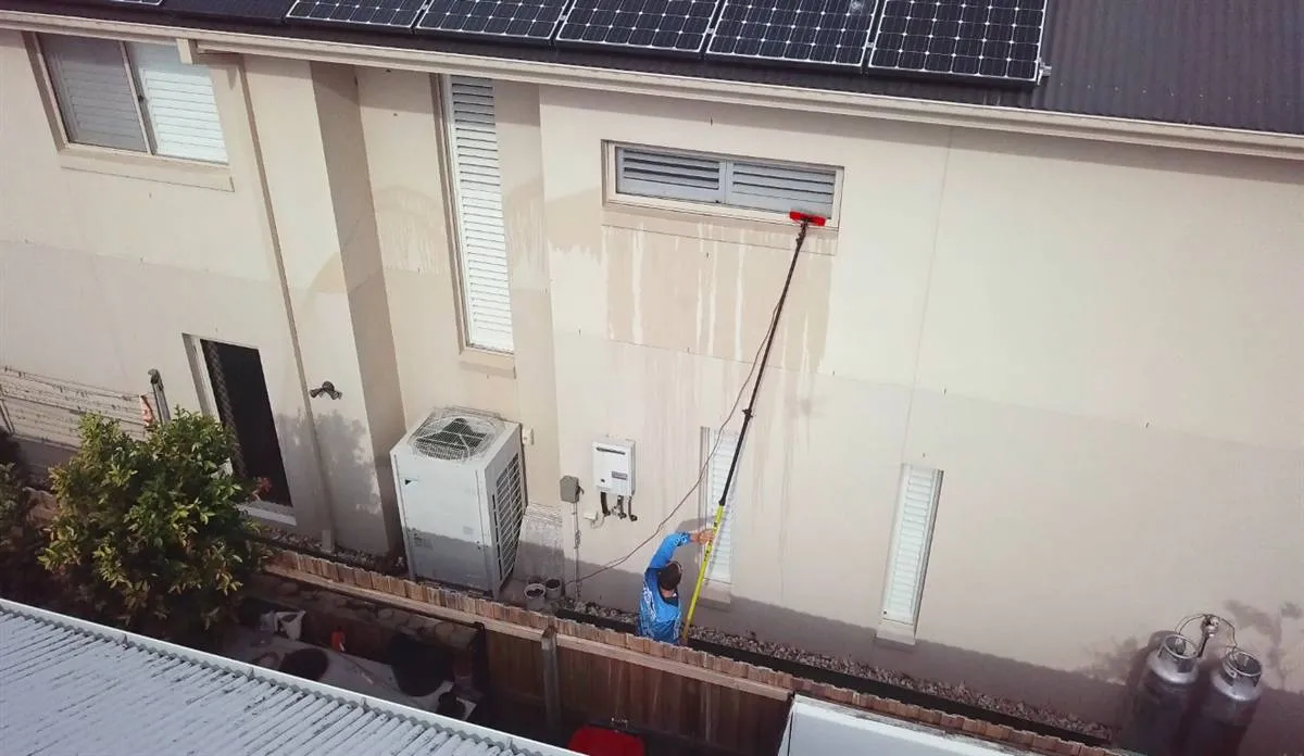 Technician soft washing an exterior surface at low pressure