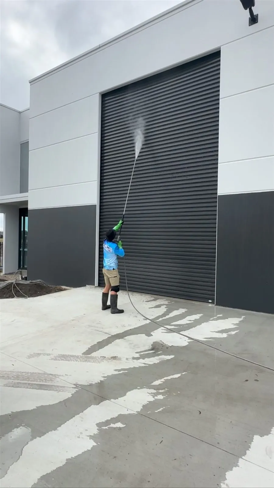 Technician pressure washing a large industrial roller door and facade