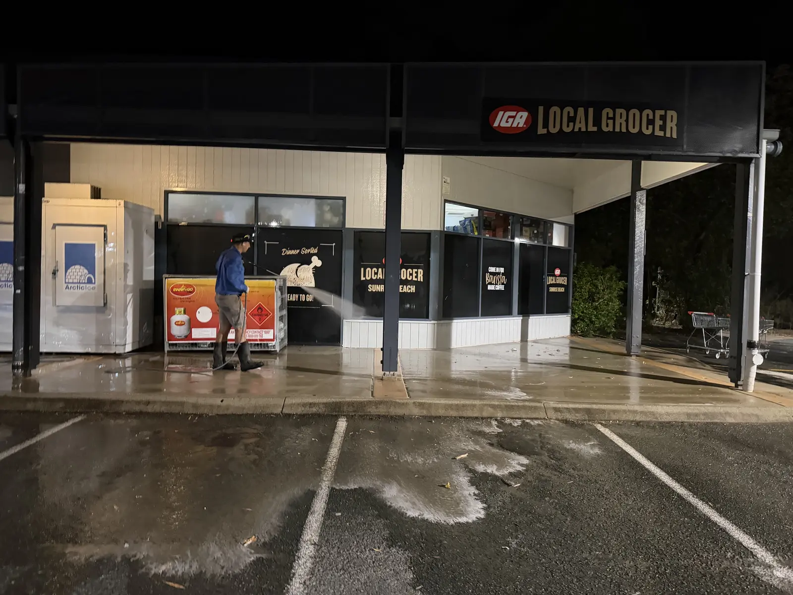Xterior Power Clean technician pressure cleaning outside the IGA Local Grocer at Sunrise Beach at night