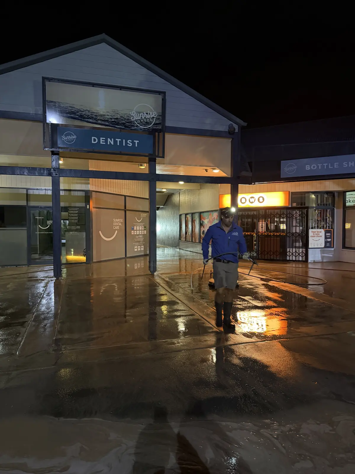 Xterior Power Clean technician pressure cleaning a shopping complex walkway at night in Sunrise Beach